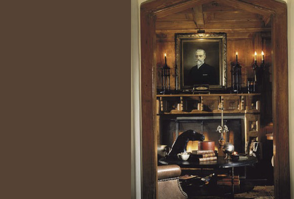 Interior view of a study with dark wood paneling, a fireplace, antique furniture, and a classic portrait painting above the mantel.