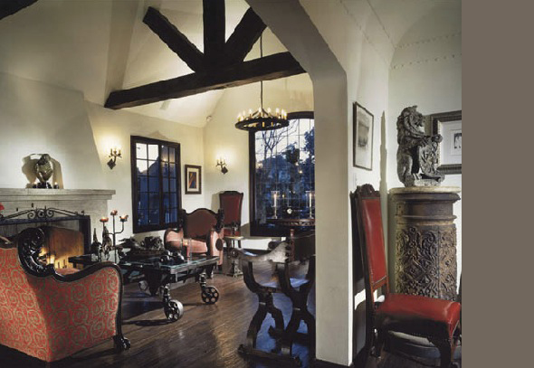 Living room featuring dark wood ceiling beams, red upholstered furniture, a lit fireplace, and decorative sculptures on the mantel and pedestal.