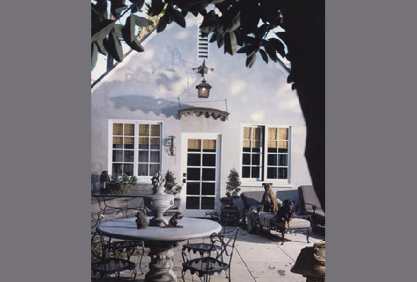 Courtyard area of the house featuring a round dining table, arched doorway, and decorative elements under tree foliage.
