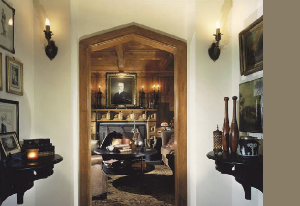 Interior view through an arched wood doorway into a living room featuring a fireplace and framed portrait above the mantle.