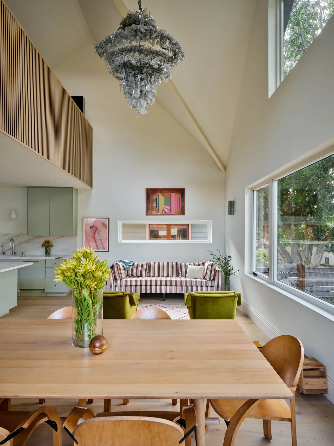 The Silver Lake Treehouse features a vaulted ceiling, green armchairs, and a striped sofa in the living area adjacent to the dining table.