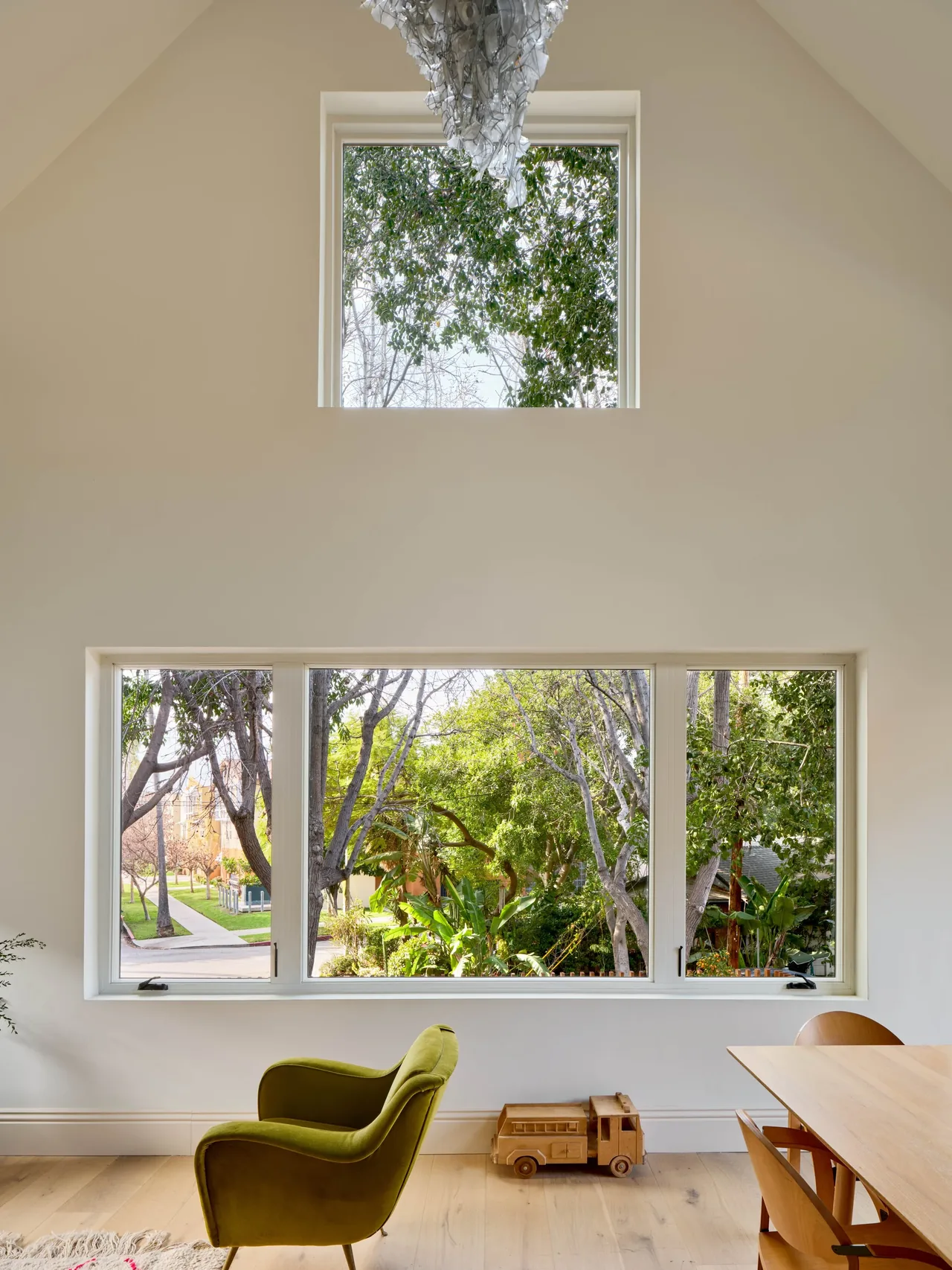 The Silver Lake Treehouse features high rectangular windows that frame a green garden view and natural wood furniture.