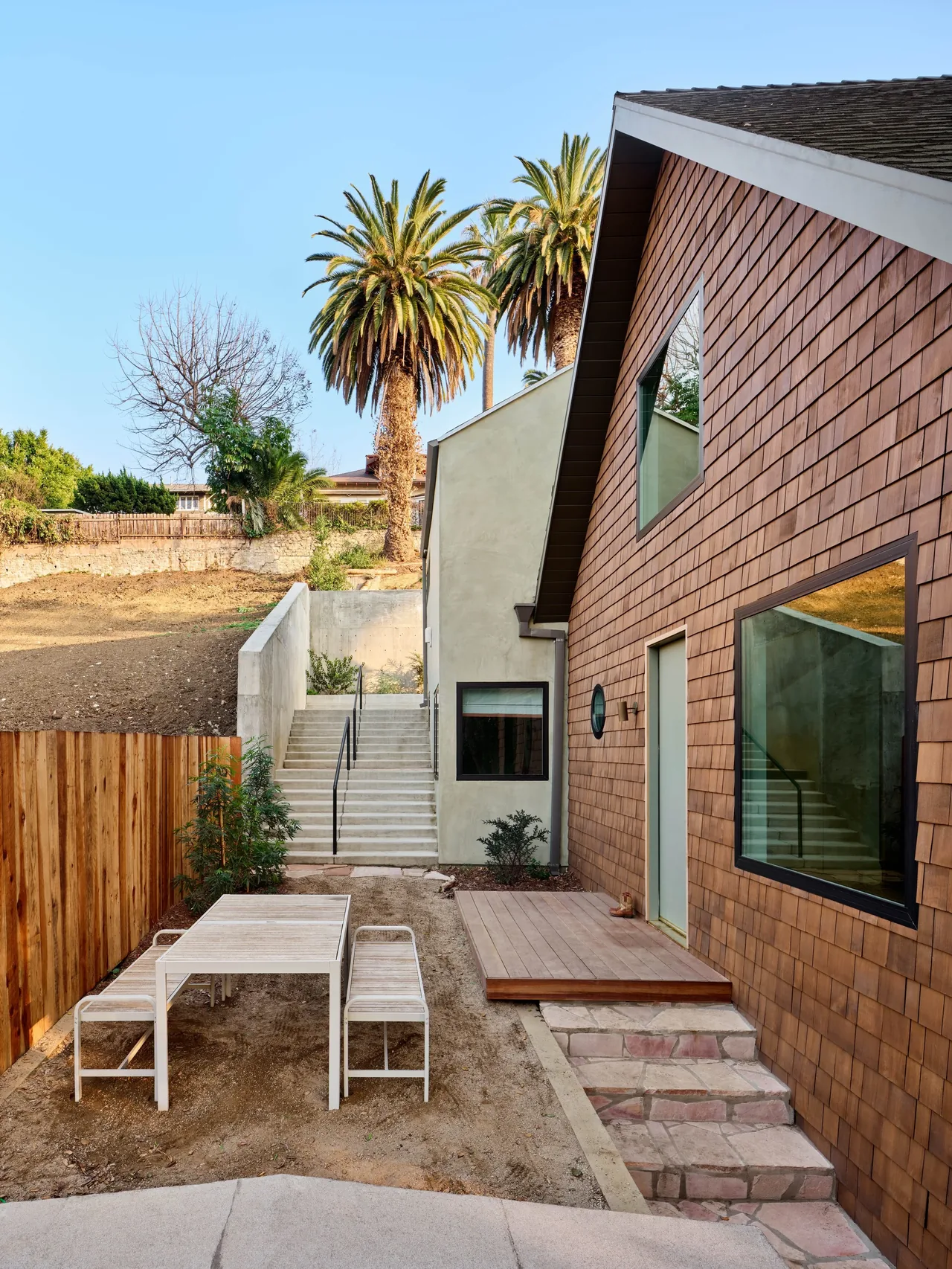 The Silver Lake Treehouse features a wood shingle exterior and a compact backyard patio with stone steps and seating area.