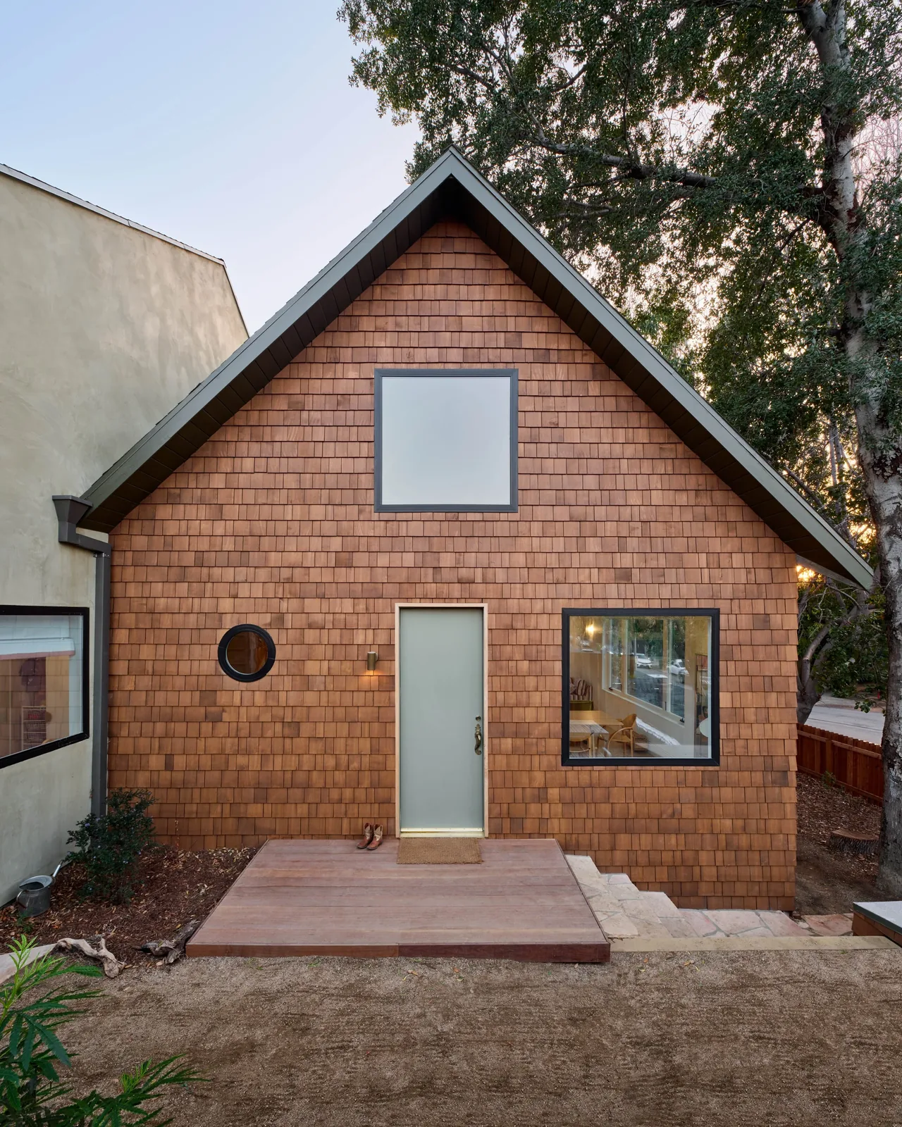 The Silver Lake Treehouse features cedar shingle siding and a gable roof, with a simple wood deck at the entrance.