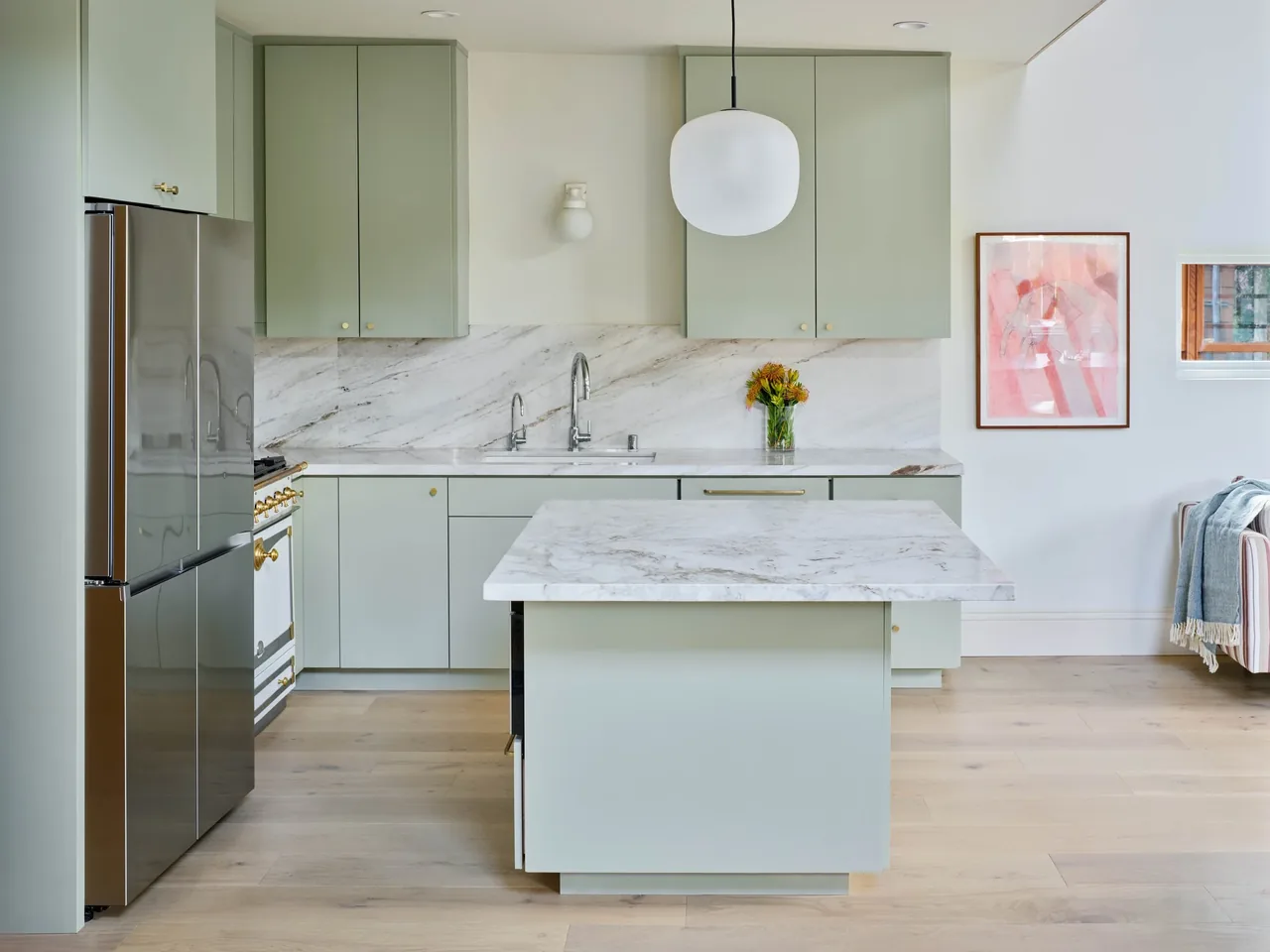 Kitchen features pale green cabinetry, marble countertops, a central island, and brass hardware.