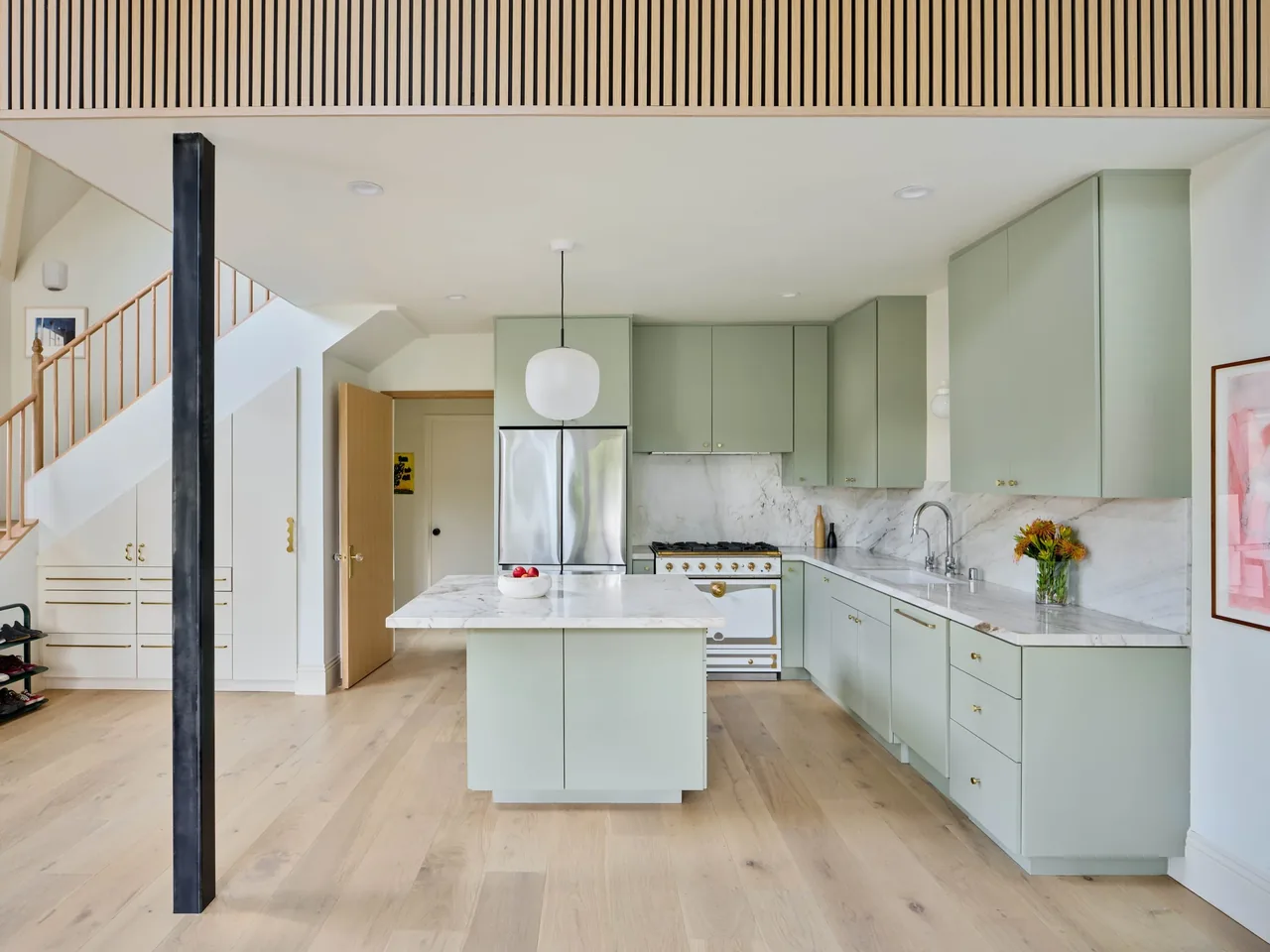 Kitchen featuring sage green cabinetry with marble countertops, a central island, and light hardwood flooring.