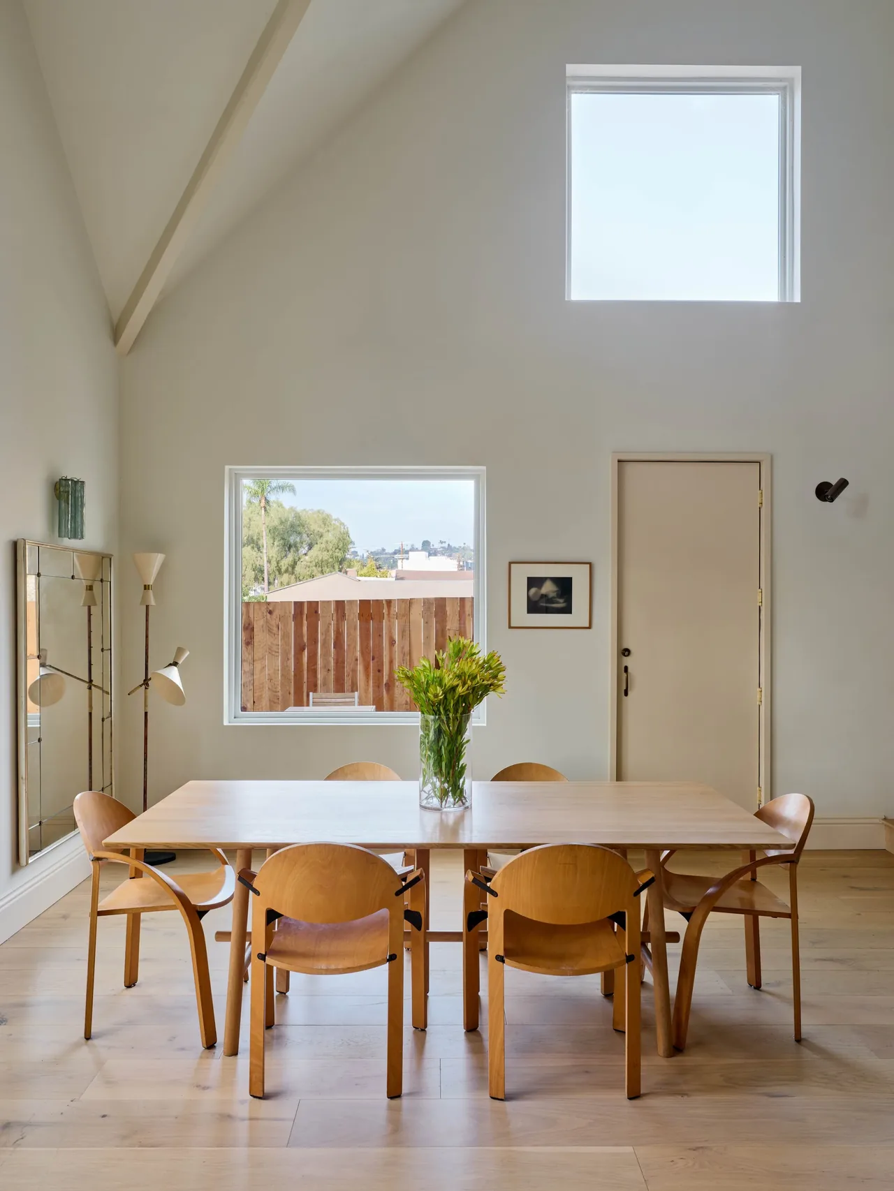 Dining room with natural wood furniture, a vaulted ceiling, and two square windows including one high on the wall.