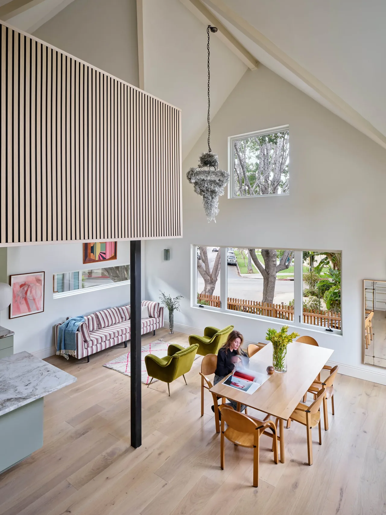 Dining and living space with vaulted ceiling and rectangular windows overlooking street trees.