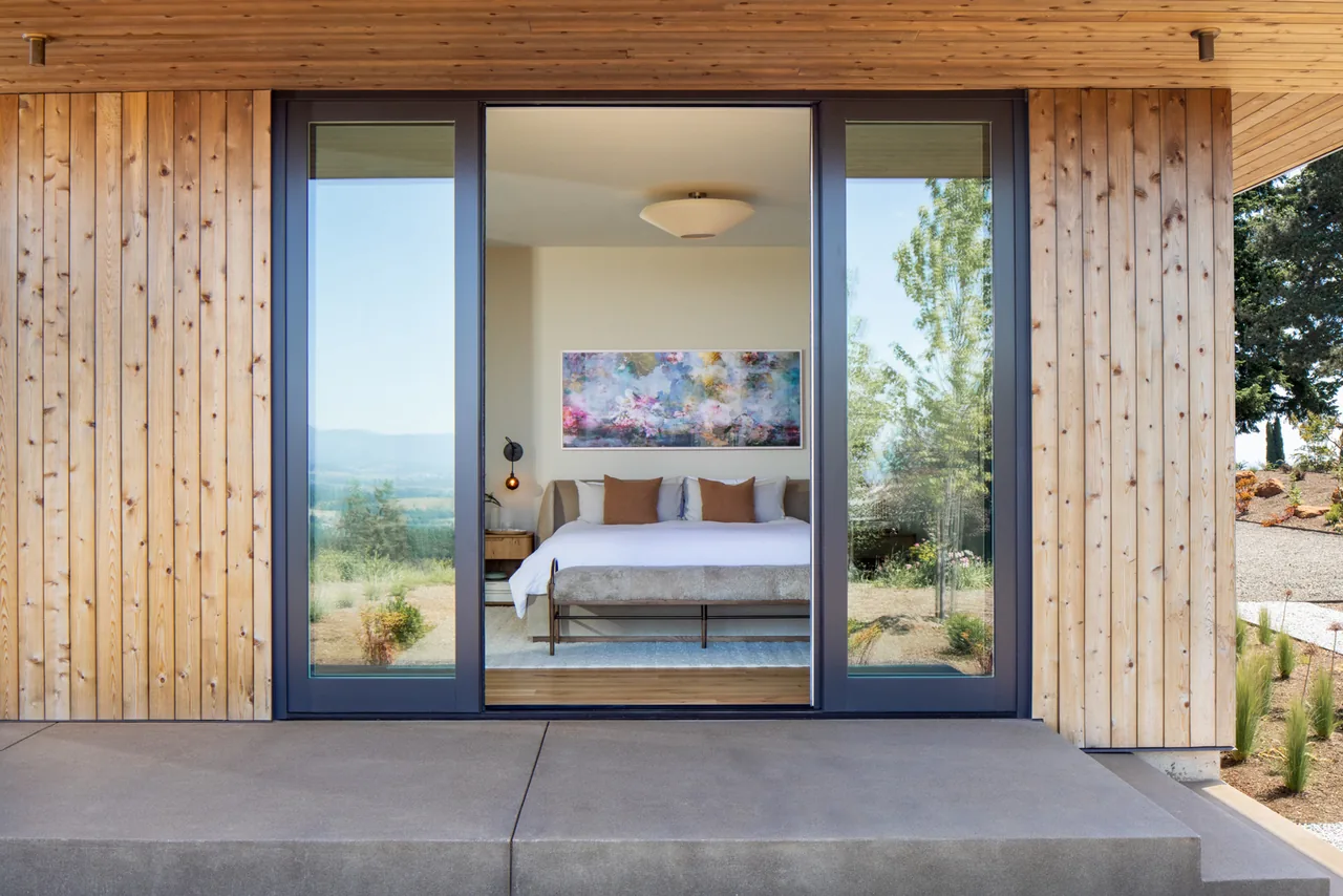 Exterior view of a bedroom with floor-to-ceiling glazing framed by natural wood siding at Hillside House by JHL Design.