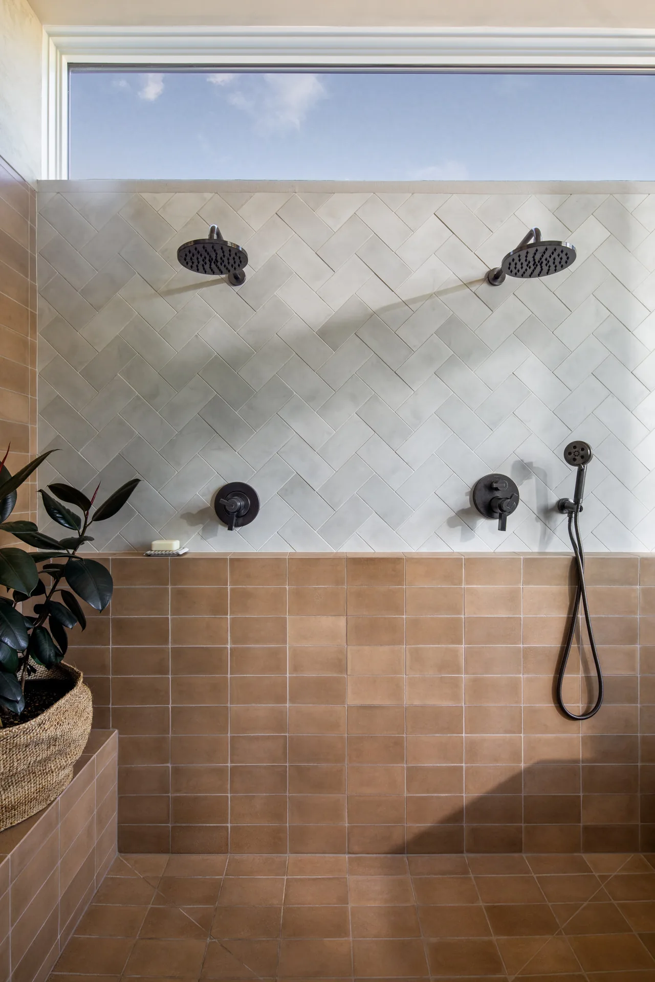 Shower space featuring dual rainfall showerheads and beige tiles with a window above providing natural light in the Hillside House project.