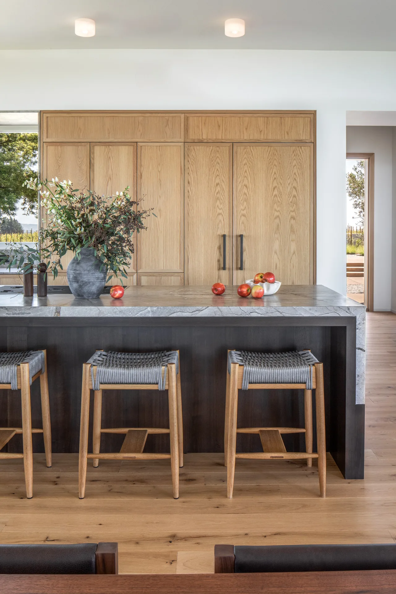 Modern kitchen features a dark island with a stone countertop and light wood cabinetry with large handles.
