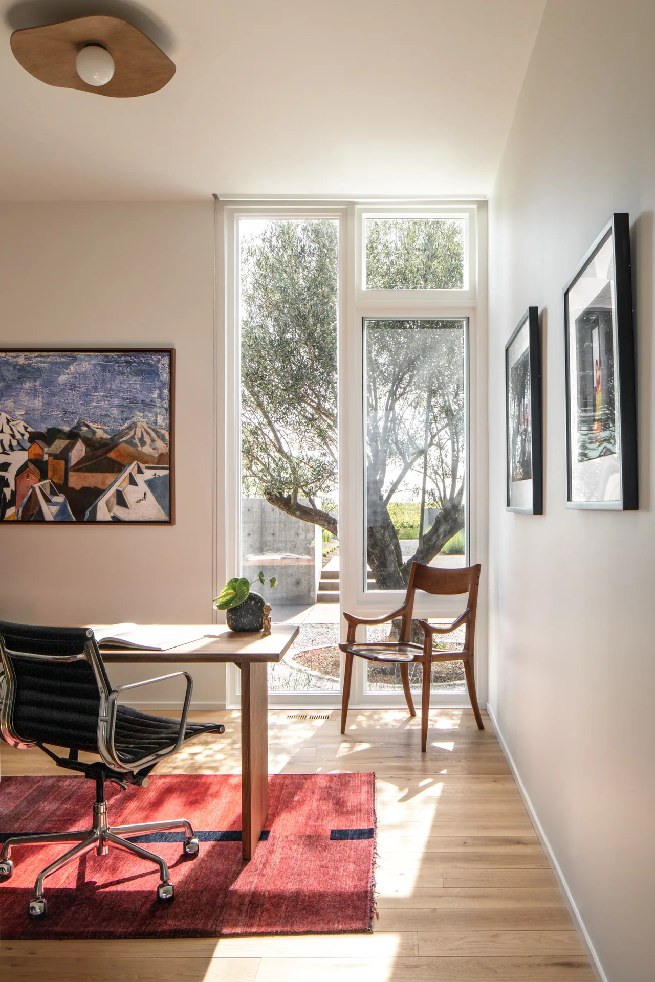 Bright home office with floor-to-ceiling windows shows outdoor tree and contemporary furnishings at Hillside House.