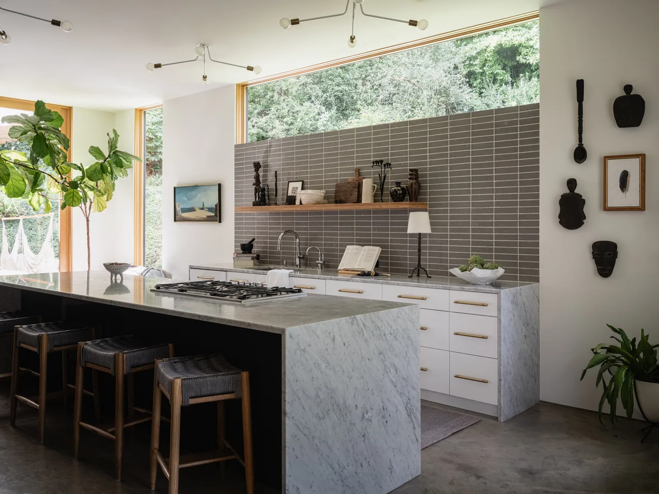 Kitchen in Idea House by JHL Design features a marble waterfall island, gray tile backsplash, and large windows overlooking greenery.