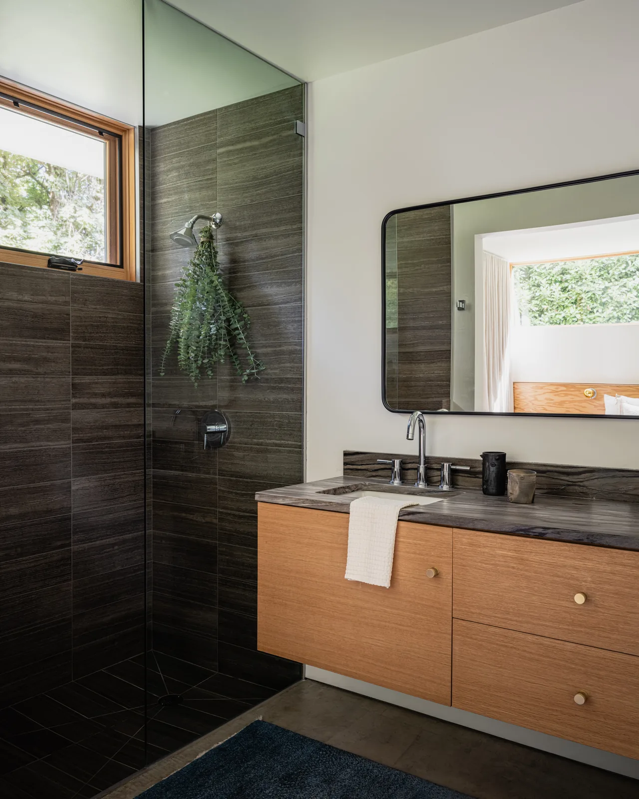Bathroom features wood cabinetry, dark tile shower with glass enclosure, and a rectangular mirror above the sink.