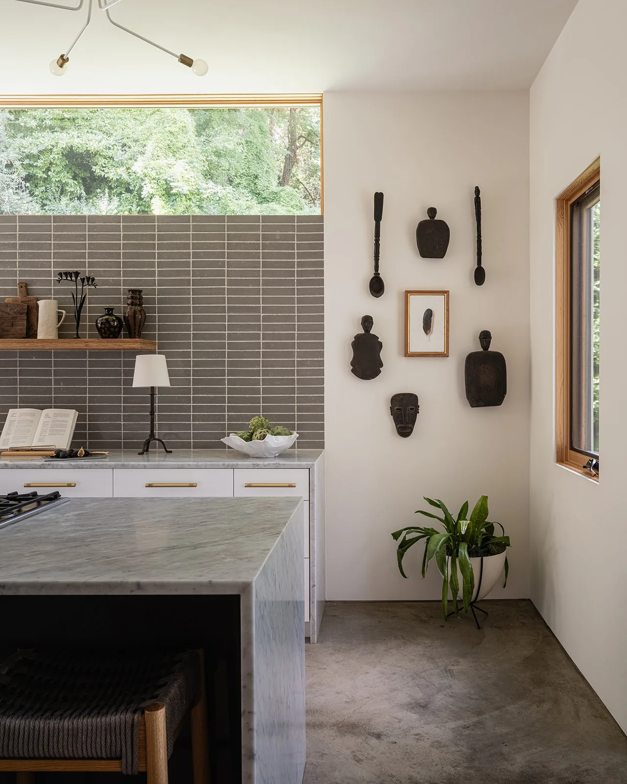 Kitchen space with gray backsplash tiles, a marble island, and decorative wooden carvings and framed feather artwork on the wall.