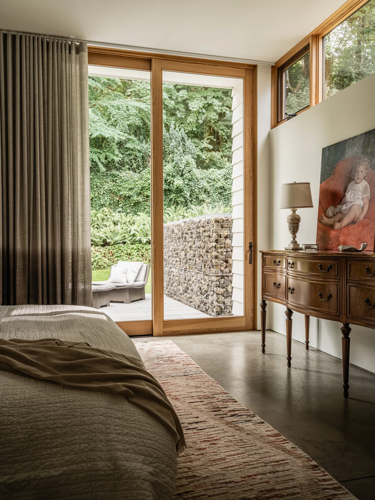 The bedroom in Idea House features a wooden sliding door leading to an outdoor seating area surrounded by greenery.