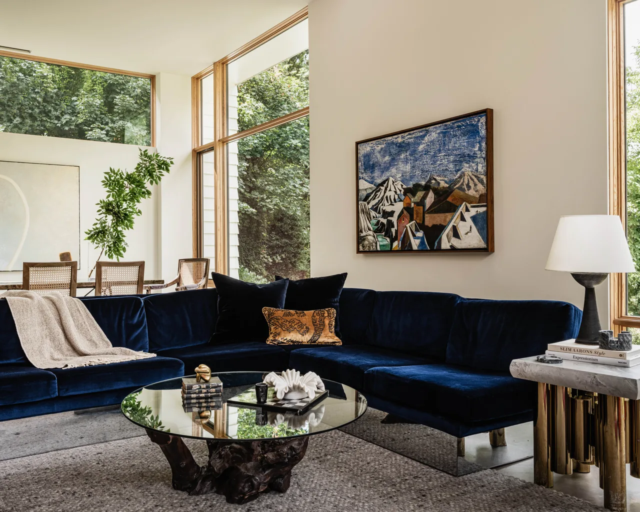 Living room in Idea House features a dark blue velvet sectional sofa and large windows with wooden frames providing garden views.