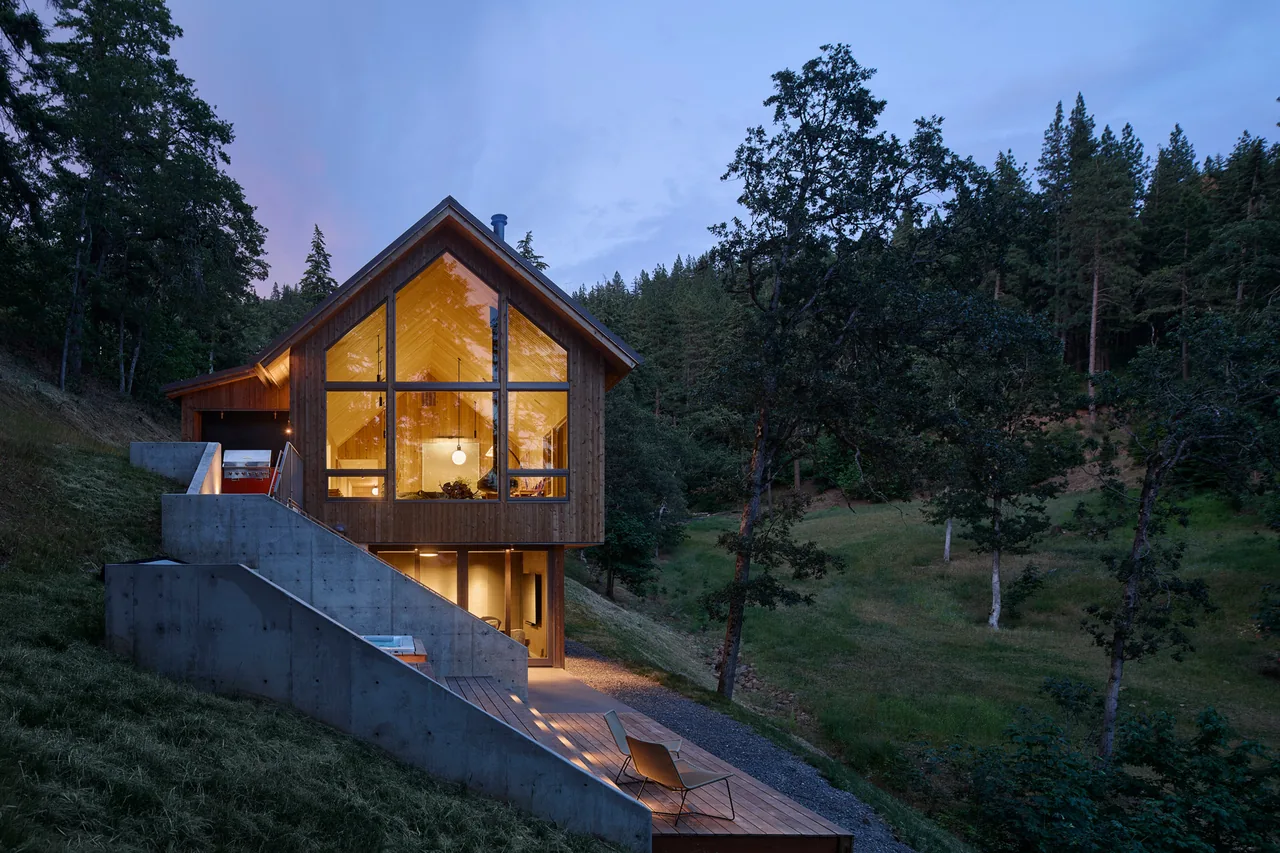 The Sanford Spring house features warm wood siding and large triangular window walls on a sloped forest site.