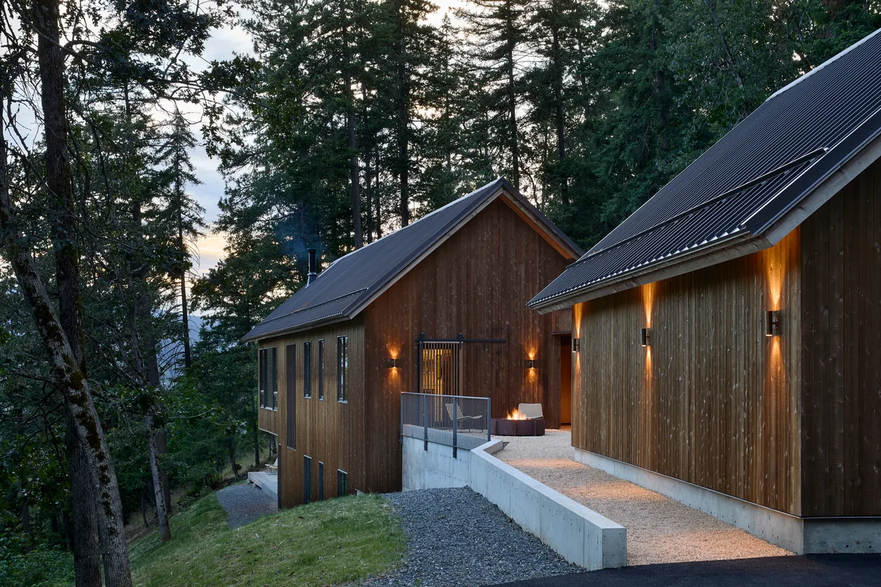 Sanford Spring project by JHL Design features connected wood buildings with metal roofs on a forest hillside with outdoor lighting.