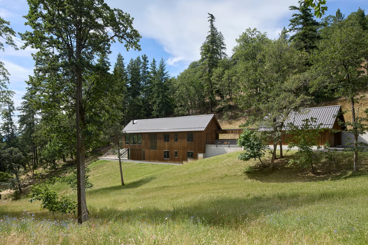 Sanford Spring features two wood-paneled structures with metal gable roofs connected by a concrete terrace in a forest hillside setting.
