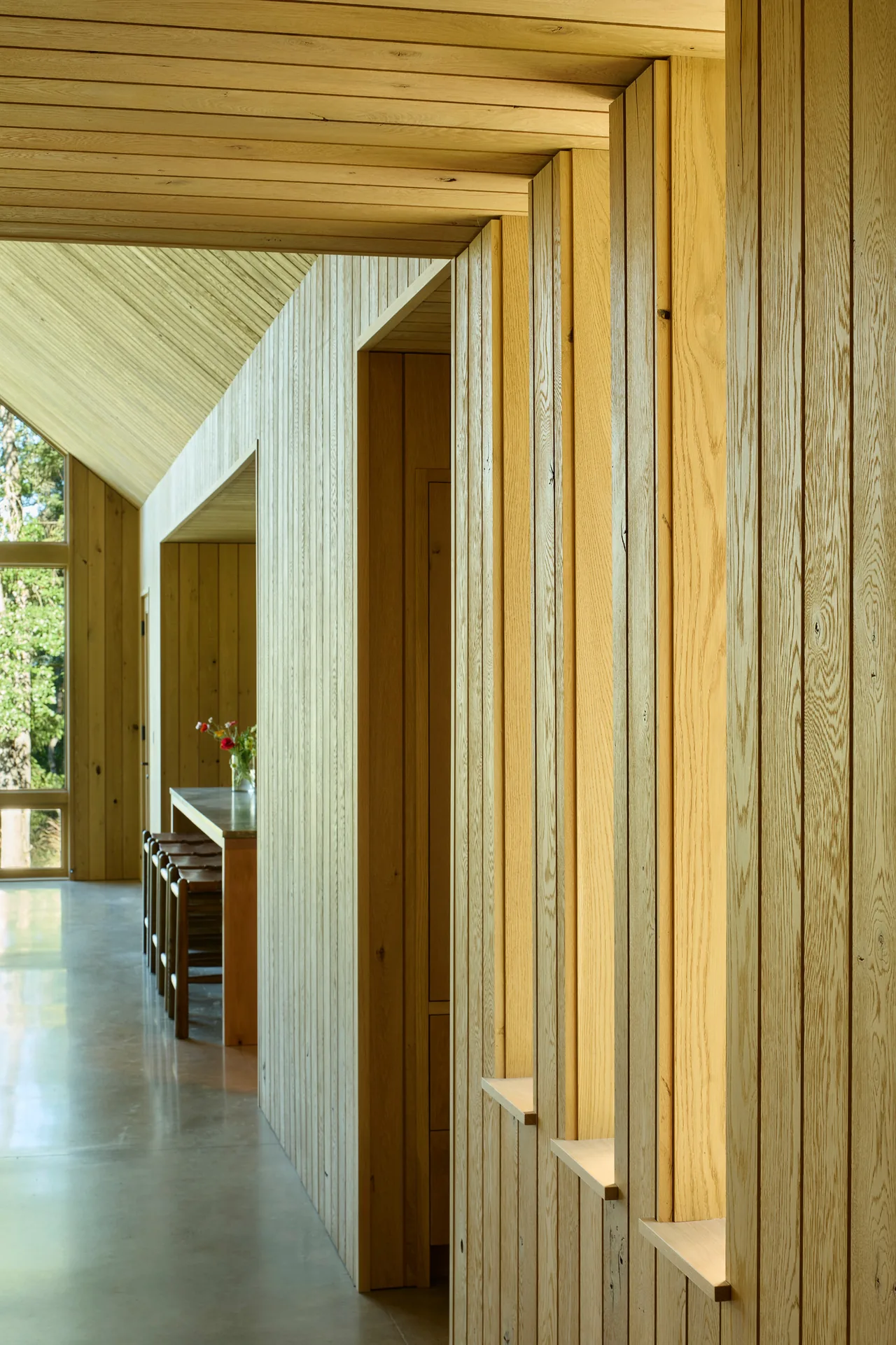 Hallway features wood paneling and connects to a dining area with extensive windows.