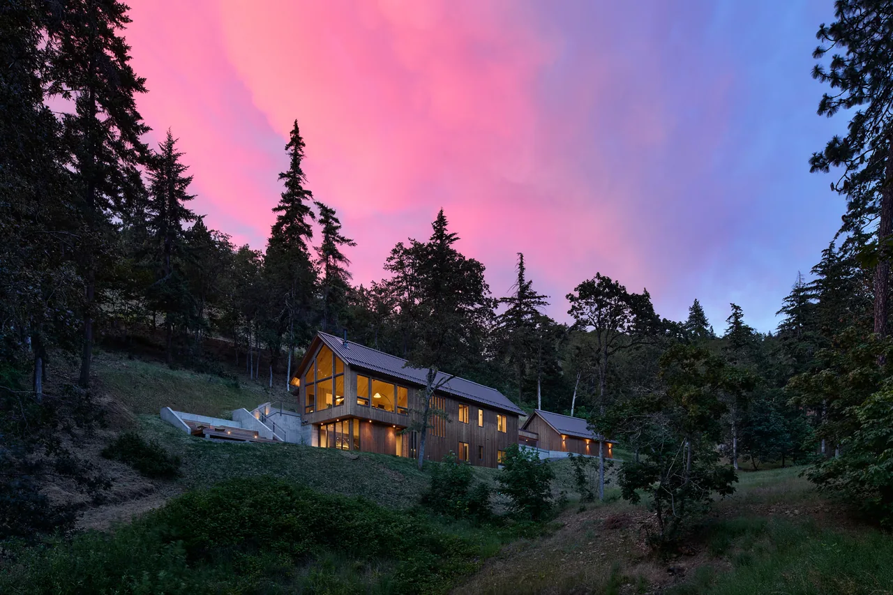 Sanford Spring house by JHL Design sits on a forested hillside with connected structures and concrete terrace seating visible.