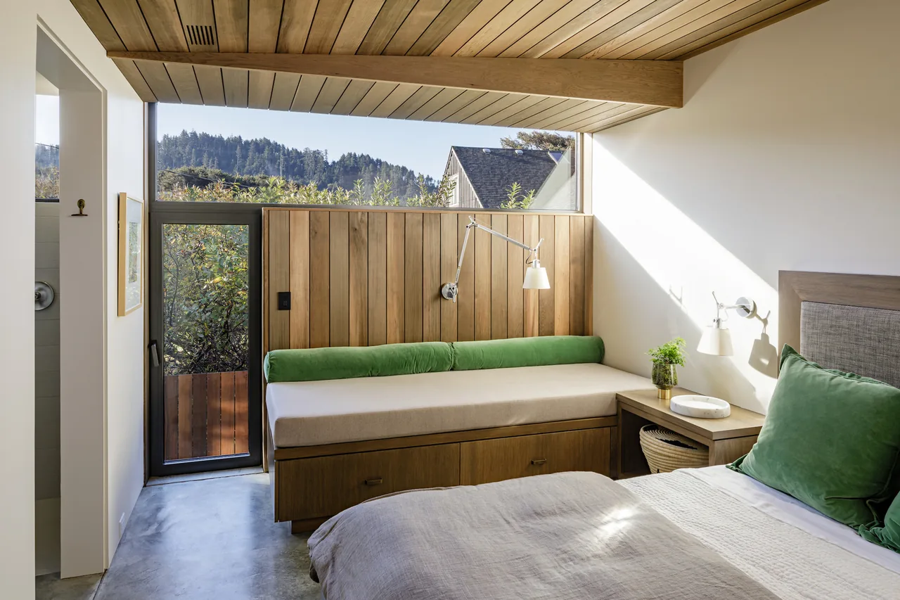 The Shelter House bedroom features a wood-paneled ceiling and wall with a green cushioned daybed and concrete flooring.