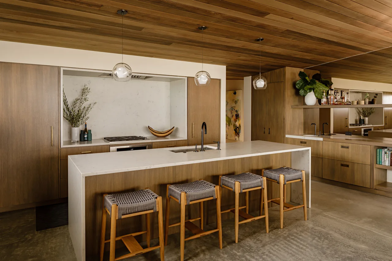 Kitchen featuring wood-paneled ceiling and cabinetry, a white island with built-in sink, and pendant lighting.