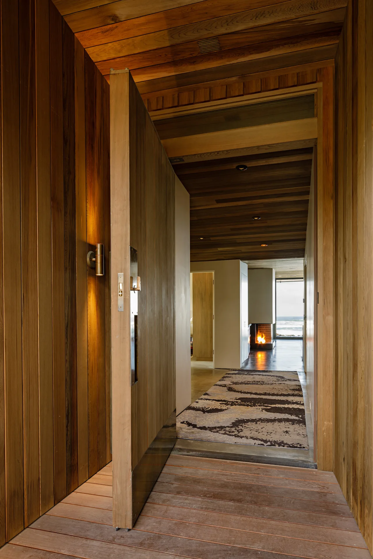 Entry hallway with wood paneling and a fireplace visible at the end overlooking water.