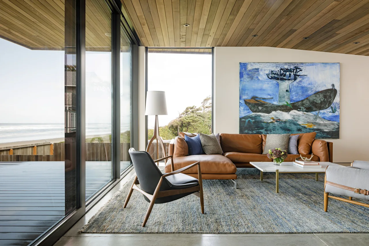 Living room with large floor-to-ceiling glazing overlooking the ocean, featuring a leather sectional sofa and wood-paneled ceiling.