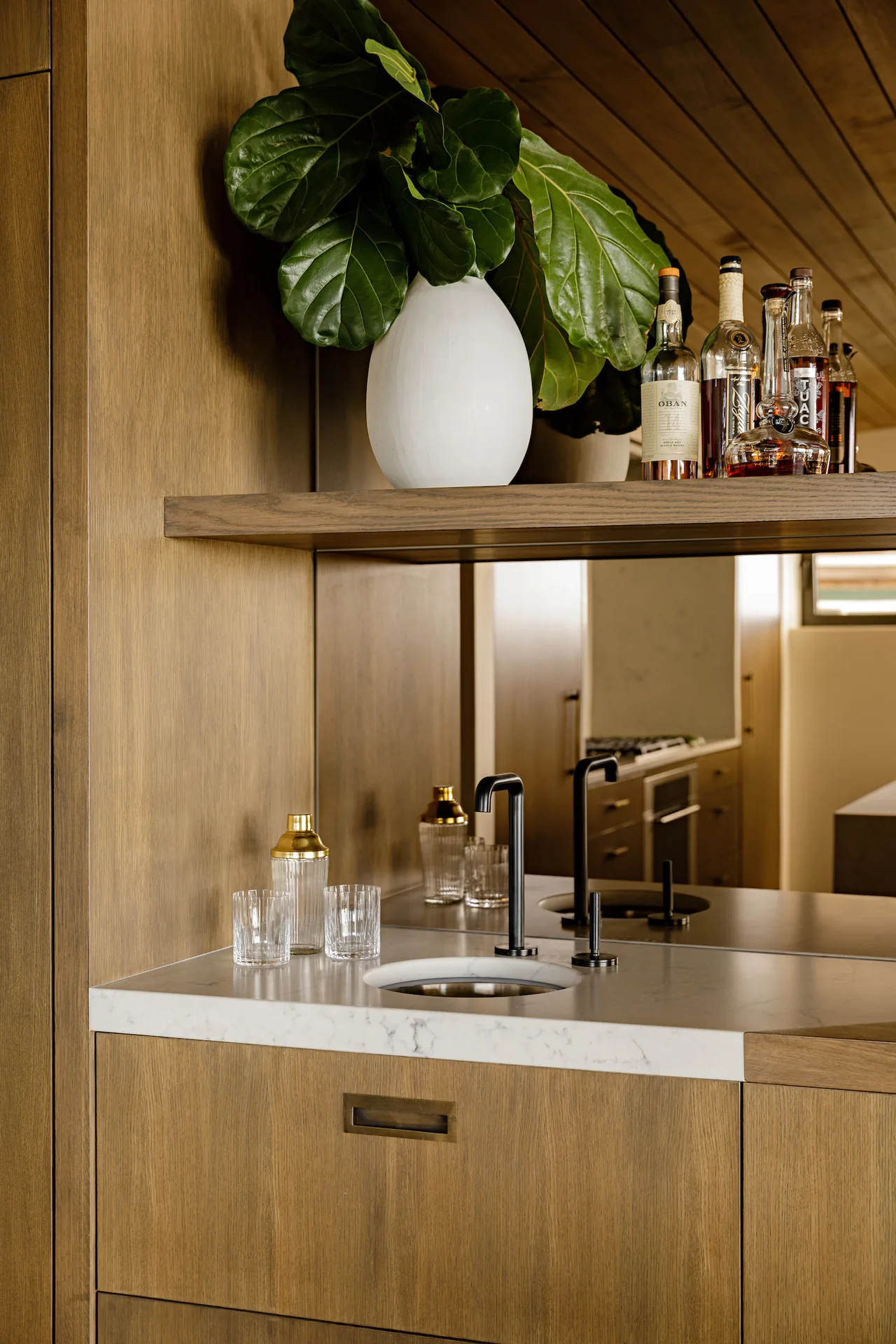 Wood-paneled bar area with a marble countertop and modern black faucet in Shelter House by JHL Design.