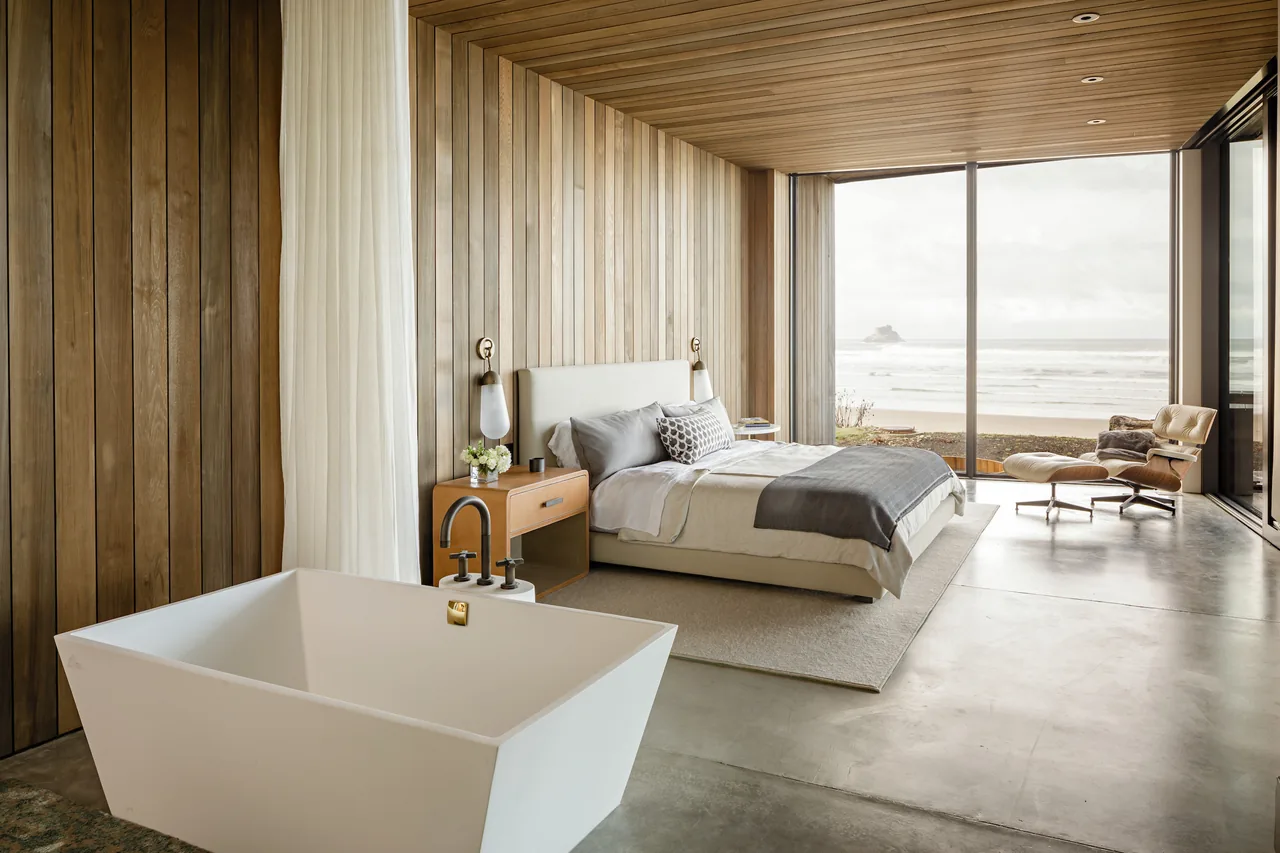 Bedroom featuring wood paneling, a freestanding tub, and floor-to-ceiling glazing overlooking the ocean at Shelter House.