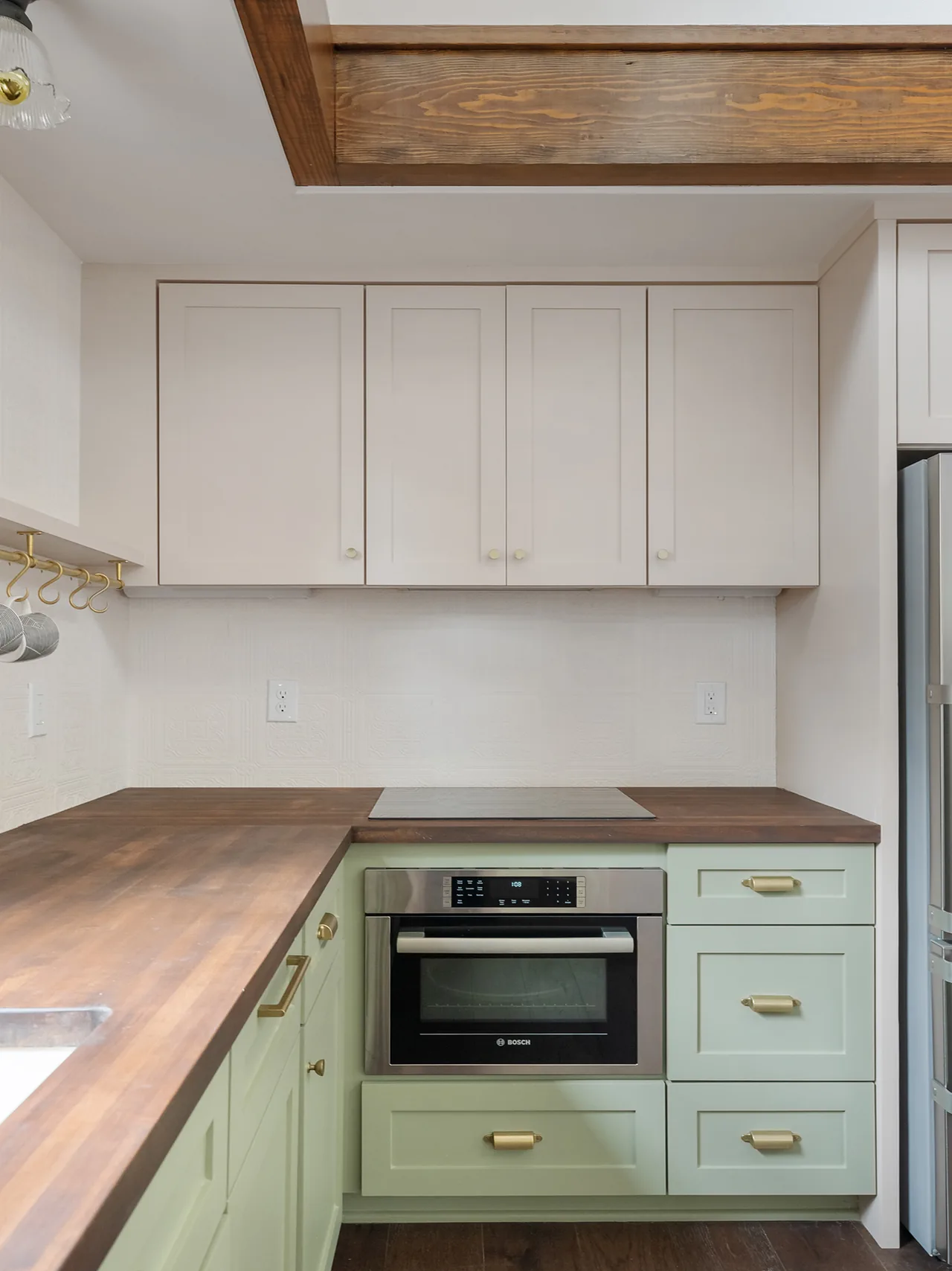 Kitchen with two-tone cabinetry featuring light green lower cabinets and cream upper cabinets, wooden countertops, and brass cabinet pulls.