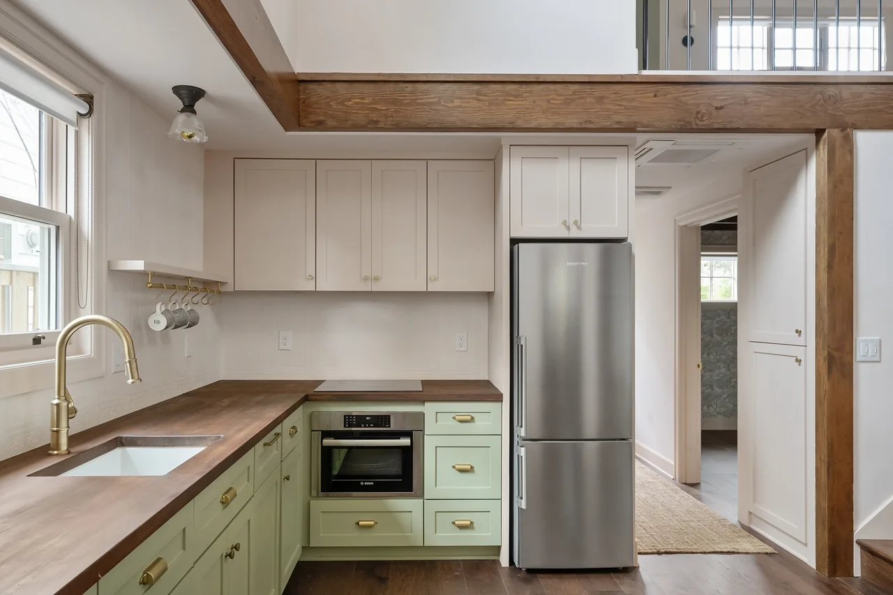 Two-tone kitchen with upper cream cabinets, lower sage green cabinets, brass hardware, and a stainless steel refrigerator in Buckman ADU.