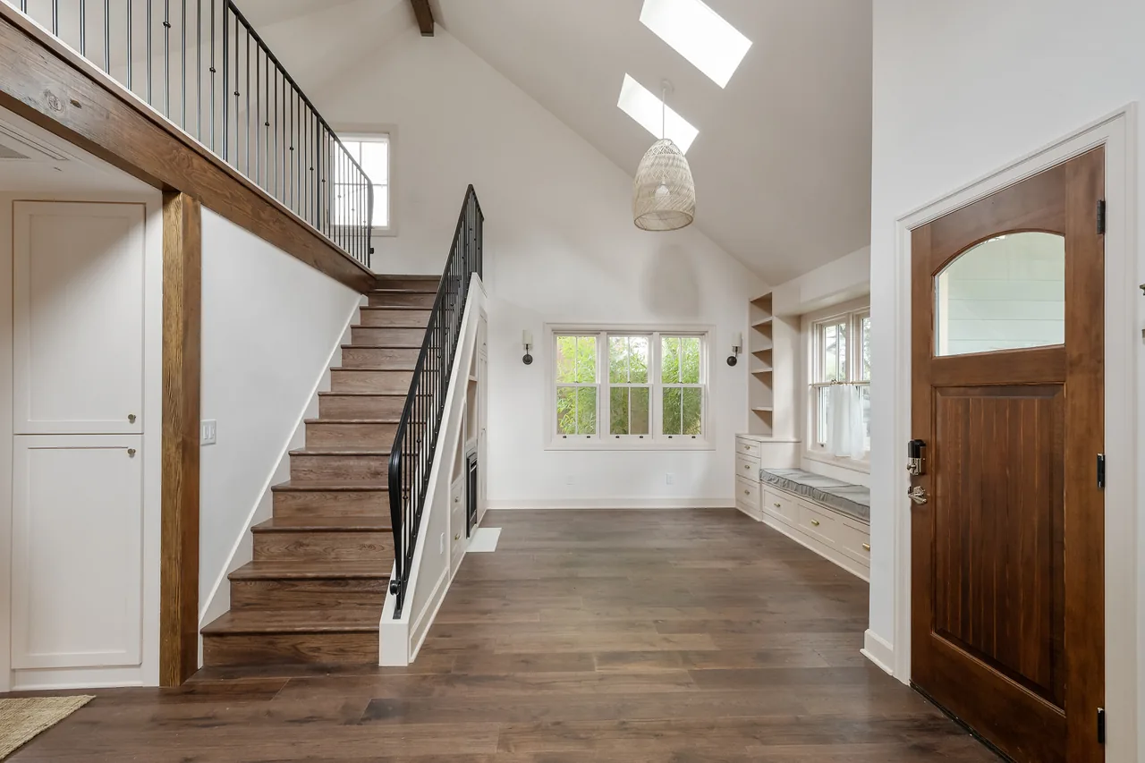 Open living area with two-story ceiling, wooden stairs, and built-in shelving beneath the staircase.
