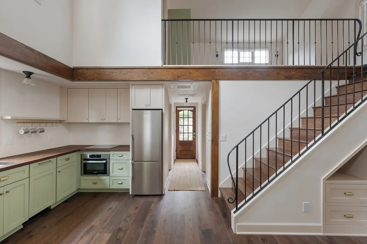 The Buckman ADU features an L-shaped kitchen with two-tone cabinetry, wooden countertops, and a metal railing along the stairway under a two-story ceiling.