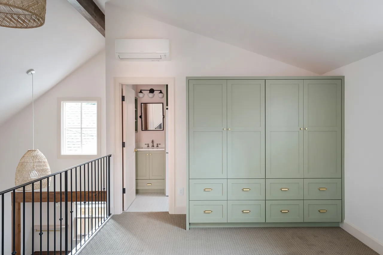Loft space in Buckman ADU featuring built-in cabinetry, a metal stair railing, and a bathroom view with matching green cabinets.