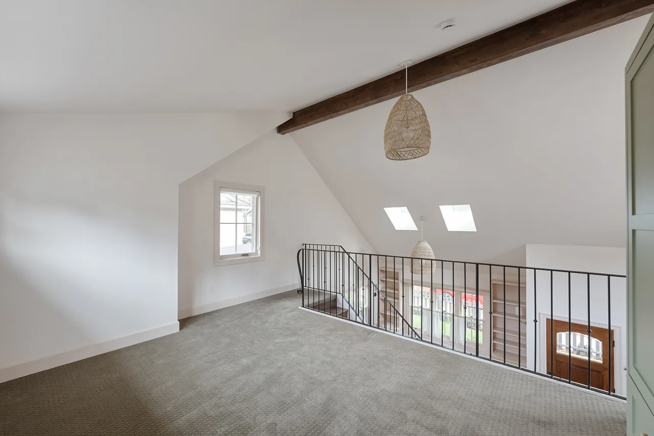 Loft area with exposed wood beam ceiling and metal railing overlooking the entry below.