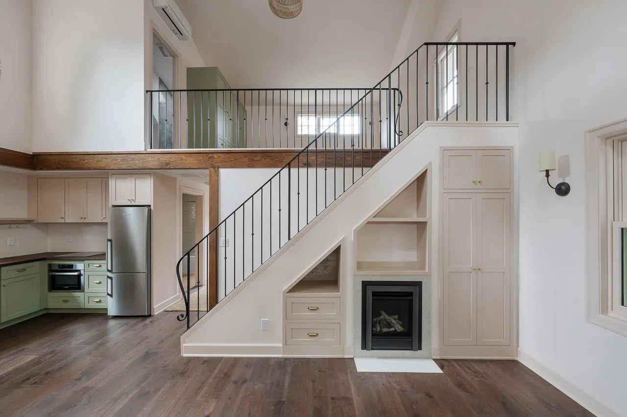 Living area with staircase featuring built-in storage and a fireplace, adjoining an L-shaped kitchen with green lower cabinets.