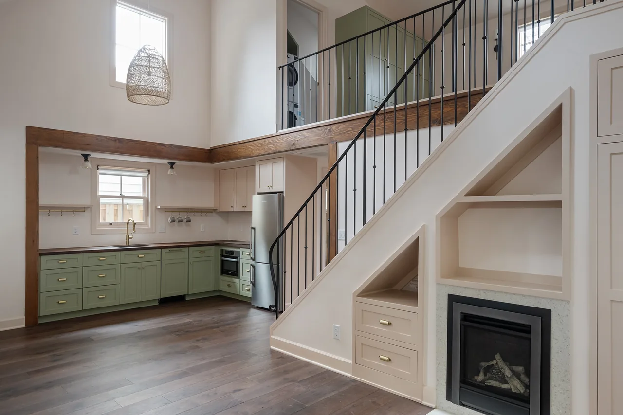 The Buckman ADU interior features a green kitchen with brass hardware, a metal stair railing, and a fireplace under the stairs.