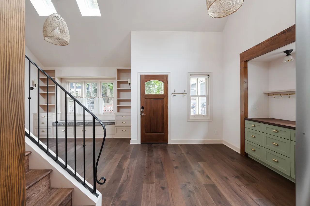 Entry room features a wood door, built-in shelving under stairs, brass cabinet pulls, and a black metal railing staircase.