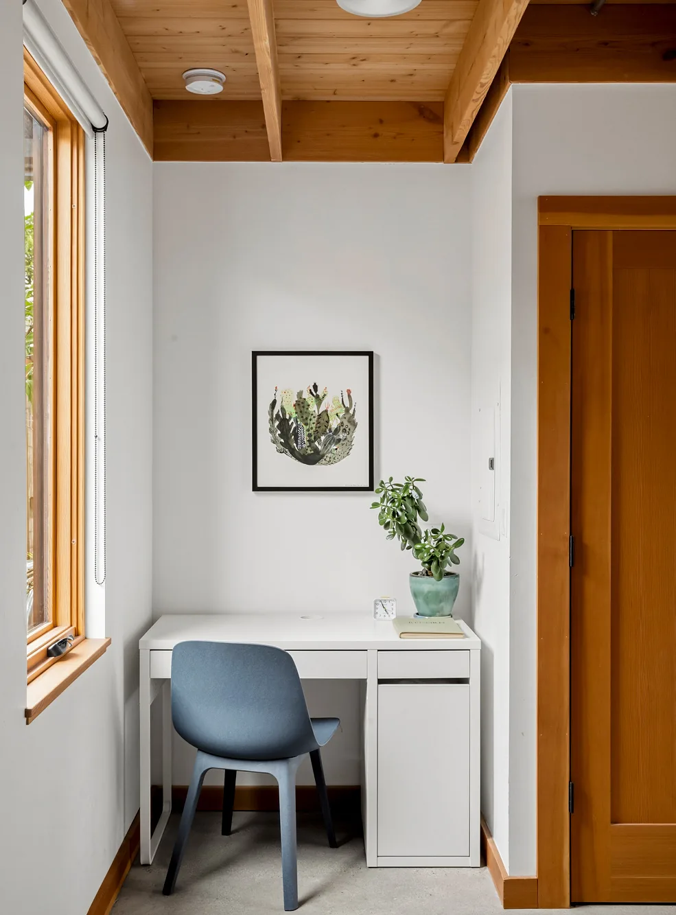 Compact office nook featuring a white desk and blue chair below exposed wood beams.
