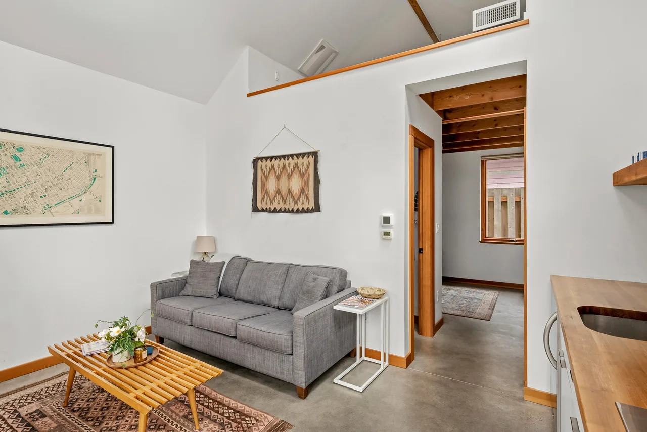 Living room of Irving Park ADU features a gray sofa, wooden coffee table, exposed wood beams, and concrete floor.