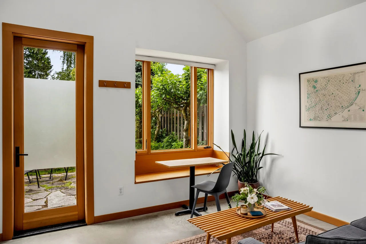 Living room features a wooden framed frosted glass door, window seat, black chair, and wooden slat coffee table.