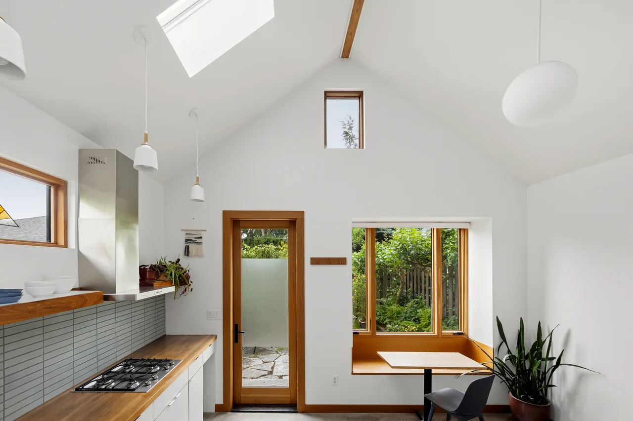 Irving Park ADU kitchen and dining nook feature a vaulted ceiling with skylight and wood-framed windows overlooking a garden.