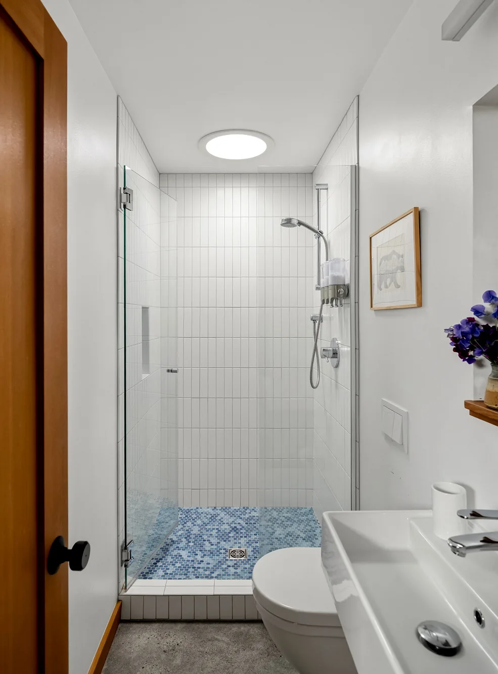 Small bathroom with glass shower enclosure and a vertical white tile shower wall with blue mosaic floor tiles.