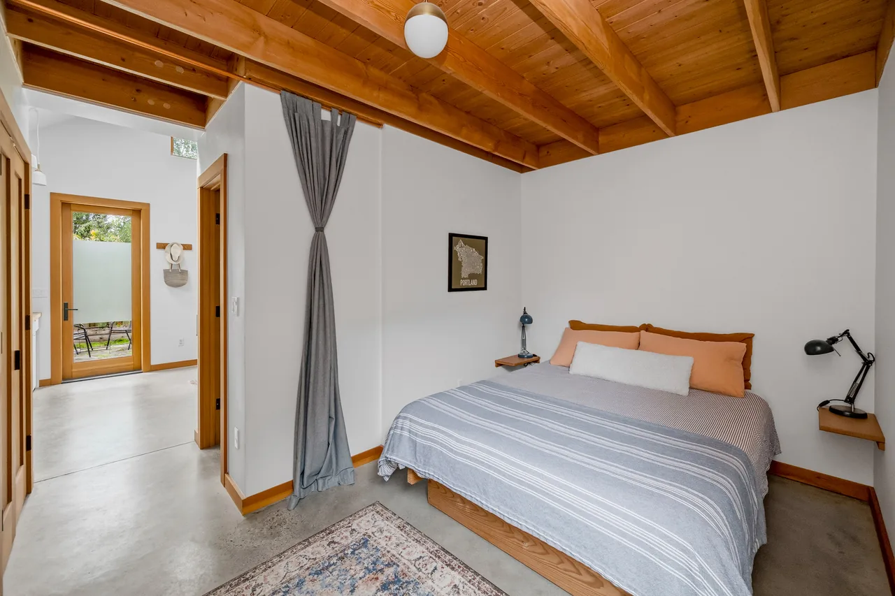 Bedroom features exposed wooden ceiling beams and a doorway with a frosted glass door opening to the outside.