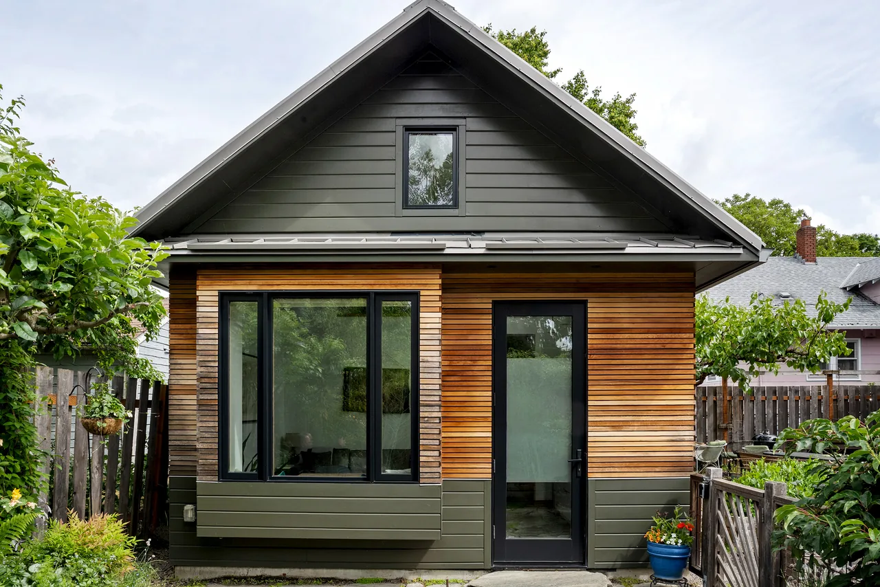 Rear view of Irving Park ADU showing mixed cladding of horizontal green siding and natural wood slats with black window and door frames.