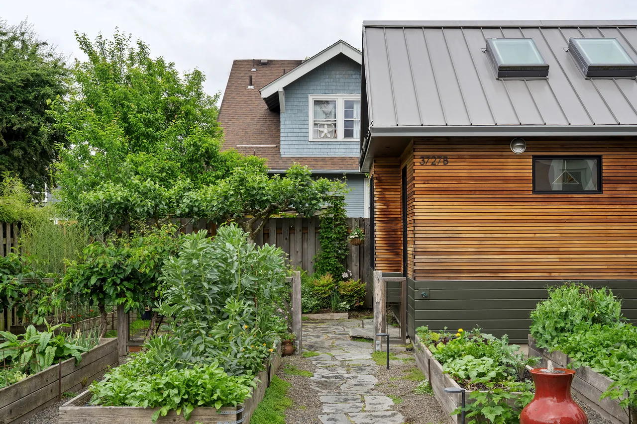 Wood-clad accessory dwelling unit features a standing seam metal roof and skylights above raised garden beds.