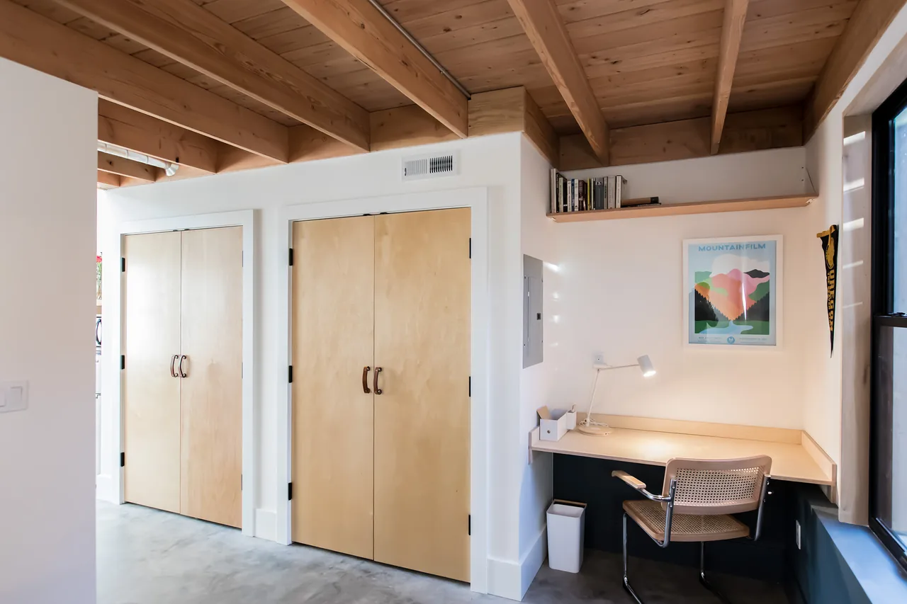 Workspace in Mason Street ADU features wood ceiling beams, light wood desk and closets, and a large side window.